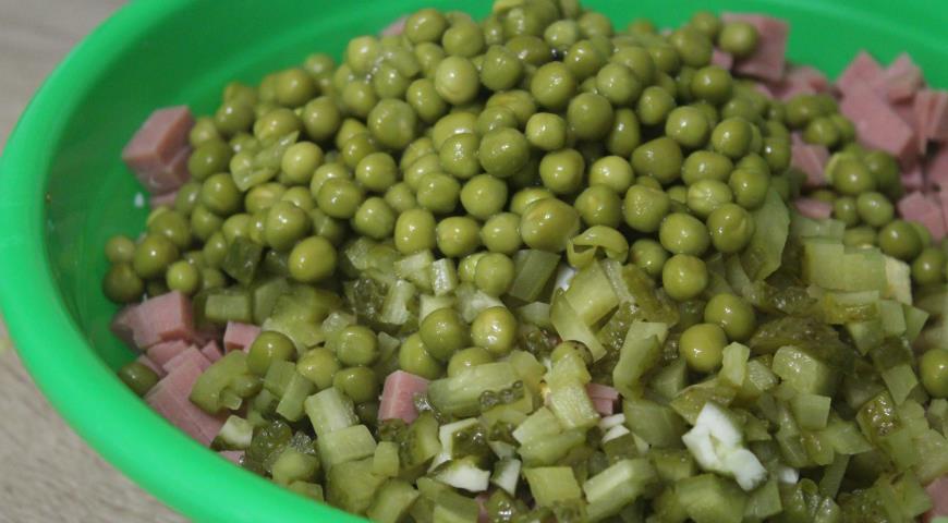 Кубиками нарезать маринованные огурцы, к оливье добавить зеленый горошек 